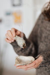 Kaboompics - Sage Smudge Stick Held over an Abalone Shell, Smoke-Filled Home Ritual