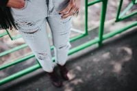 Kaboompics - Blonde woman in a black jacket and ripped jeans by a green handrail