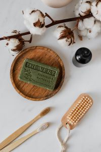 Kaboompics - Olive Soap and Amber Bottle with Cotton Branch on Wooden Tray, Organic Bath and Body Still Life