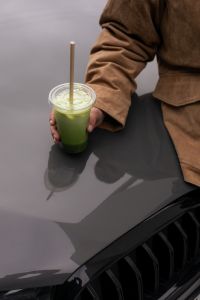 Kaboompics - Woman Holding Iced Matcha Over a Rainy Car Hood
