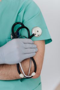 Kaboompics - Gloved Hand Holding a Stethoscope Against Mint Scrubs, Close-Up Medical Training Image