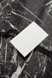 Kaboompics - White Business Card Mockup Entering from Lower Edge of Black Marble, Copy Space