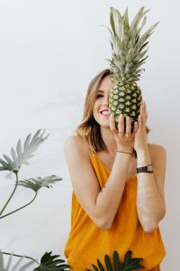 Kaboompics - Woman Holding Pineapple in Front of Her Face, Smiling Yellow Top Portrait on White