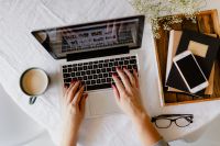 Kaboompics - Woman Typing on MacBook in Bed with Coffee, Smartphone and Books in a Cozy Home Office
