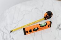 Kaboompics - Orange Spirit Level and Yellow Tape Measure beside Wall Anchors on White Marble