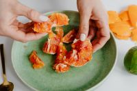 Kaboompics - A woman peels an orange on a green plate