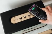 Kaboompics - Black speaker on marble table, white wall, mobile phone in hand
