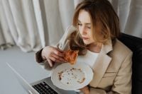Close-Up of Hands Breaking a Croissant beside a Laptop