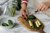 Kaboompics - Hands Slicing Cucumbers on a Wooden Cutting Board with a Glass Jar