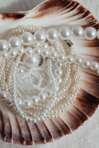 Kaboompics - Pearl Necklace Draped Across a Large Scallop Shell on Neutral Fabric, Vertical Close-Up