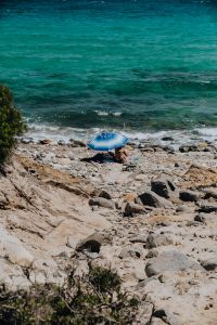 Kaboompics - Woman Relaxing Under a Blue Beach Umbrella on a Rocky Shore