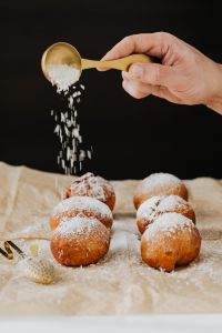 Kaboompics - Close-Up of a Gold Spoon Pouring Icing Sugar over Homemade Doughnuts