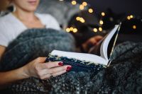 Kaboompics - Woman Reading an Open Book While Reclining Under a Gray Knit Blanket