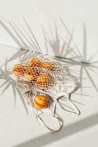 Kaboompics - Reusable Produce Bag of Oranges on a Sunlit White Surface with Palm Shadows