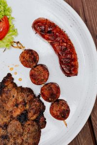 Kaboompics - Whole Grilled Sausage and Pork Neck Steak with Sausage Medallions on White Plate