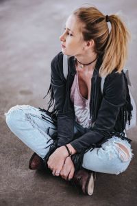 Kaboompics - Blonde woman in a black jacket and ripped jeans by a green handrail
