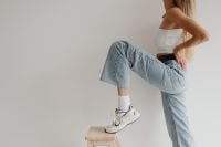 Kaboompics - Woman Sitting with Raised Knee in Wide-Leg Jeans, White Top and Sneakers, Studio Fashion Portrait