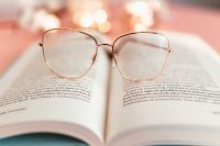 Kaboompics - Reading Glasses on an Open Book with Warm Pink Candle Bokeh