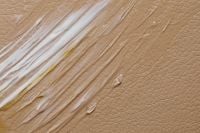 Kaboompics - Long White and Pale Yellow Cream Streaks Across Tan Pebbled Surface, Skincare Macro