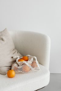 Kaboompics - Reusable Citrus Grocery Bag and Loose Oranges on a Cream Armchair