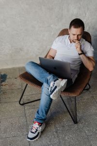 The man is sitting in a chair and working with a laptop