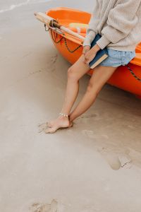 Kaboompics - Barefoot Woman Seated on an Orange Kayak with a Book at the Sandy Seashore