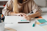 Kaboompics - Graphic Designer Drawing in a Sketchbook with Color Swatches on a White Workspace