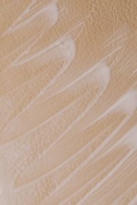 Kaboompics - Broad White Skincare Cream Strokes Across Tan Pebbled Surface, Abstract Macro