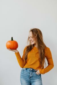 Kaboompics - Smiling Woman Holding Pumpkin in Orange Sweater