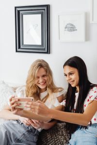 Kaboompics - Vertical Portrait of Teen Girls Taking a Phone Selfie Together on a Sofa