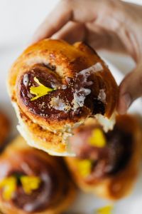 Kaboompics - Hand Holding Cinnamon Roll with Yellow Edible Flower for Bakery Lifestyle Content