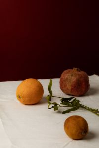 Kaboompics - Pomegranate and Citrus Still Life with Green Stem, Burgundy Backdrop