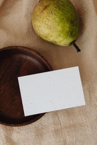 Kaboompics - Green Pear and Blank Card with Dark Wooden Plate on Beige Linen