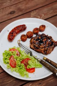 Kaboompics - Vertical Barbecue Plate with Grilled Pork Neck, Sausages and Tomato Lettuce Salad