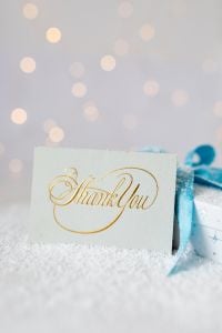 Kaboompics - White Christmas Gift with Blue Bow beside Gold Thank You Card, Bokeh Background