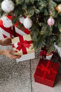 Kaboompics - Hands Holding a Gold Christmas Gift Under a Decorated Tree