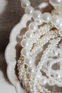 Kaboompics - Close Crop of Layered Pearl Necklaces in Scalloped Dish Against Dark Woven Background