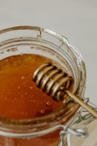 Kaboompics - Vertical Honey Jar Close-Up with Wooden Dipper and Pale Copy Space, Food Background