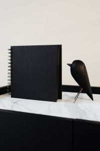 Kaboompics - Upright Black Spiral Notebook and Wooden Bird Decor on a Marble Console