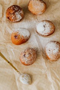 Kaboompics - Overhead Arrangement of Sugar-Dusted Polish Paczki and Gold Sifter on Cream Tablecloth