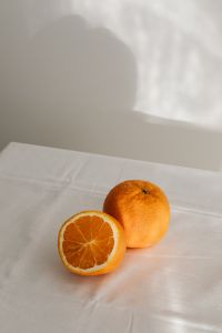 Kaboompics - Whole and Halved Orange in Soft Window Light, Minimal Citrus Still Life on White Linen