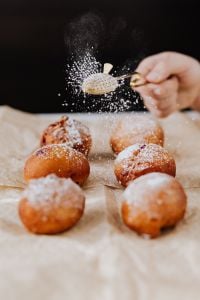 Kaboompics - Hand Sifting Powdered Sugar over Polish Paczki Doughnuts against a Dark Studio Background