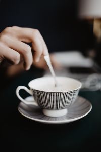 Kaboompics - Hand Stirring Coffee beside Laptop and Earbuds, Vertical Home Office Close-Up