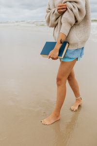 Kaboompics - Woman Walking Along the Seashore with a Blue Book and Visible Forearm Tattoo, Beach Lifestyle