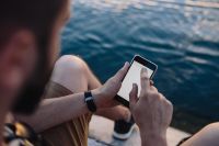 Kaboompics - Man Tapping a Smartphone Beside the Sea in a Close Seated Crop