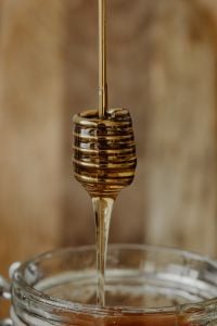 Kaboompics - Vertical Close-Up of Honey Dipper Dripping into a Glass Jar, Soft-Focus Kitchen Background