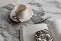 Kaboompics - White Coffee Cup, Open Planner and Silver Smartphone on Marble, Metallic Home Office Still Life