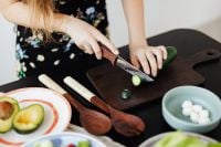 Kaboompics - Close-Up of Woman Slicing Cucumber on a Dark Cutting Board