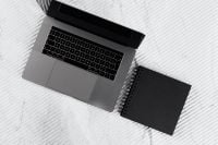 Kaboompics - Black Spiral Notebook beside Laptop on White Marble Desk, Minimalist Workspace Flat Lay