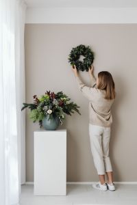 Kaboompics - Woman Hanging a Christmas Wreath on a Neutral Wall